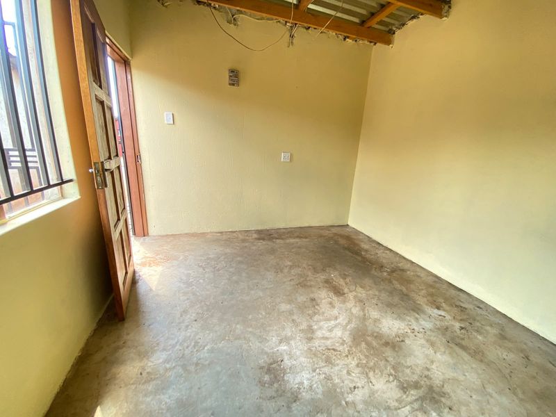An unfinished bedroom space featuring exposed ceiling beams, concrete flooring, and a timber door, offering a blank canvas for renovation and interior finishing.