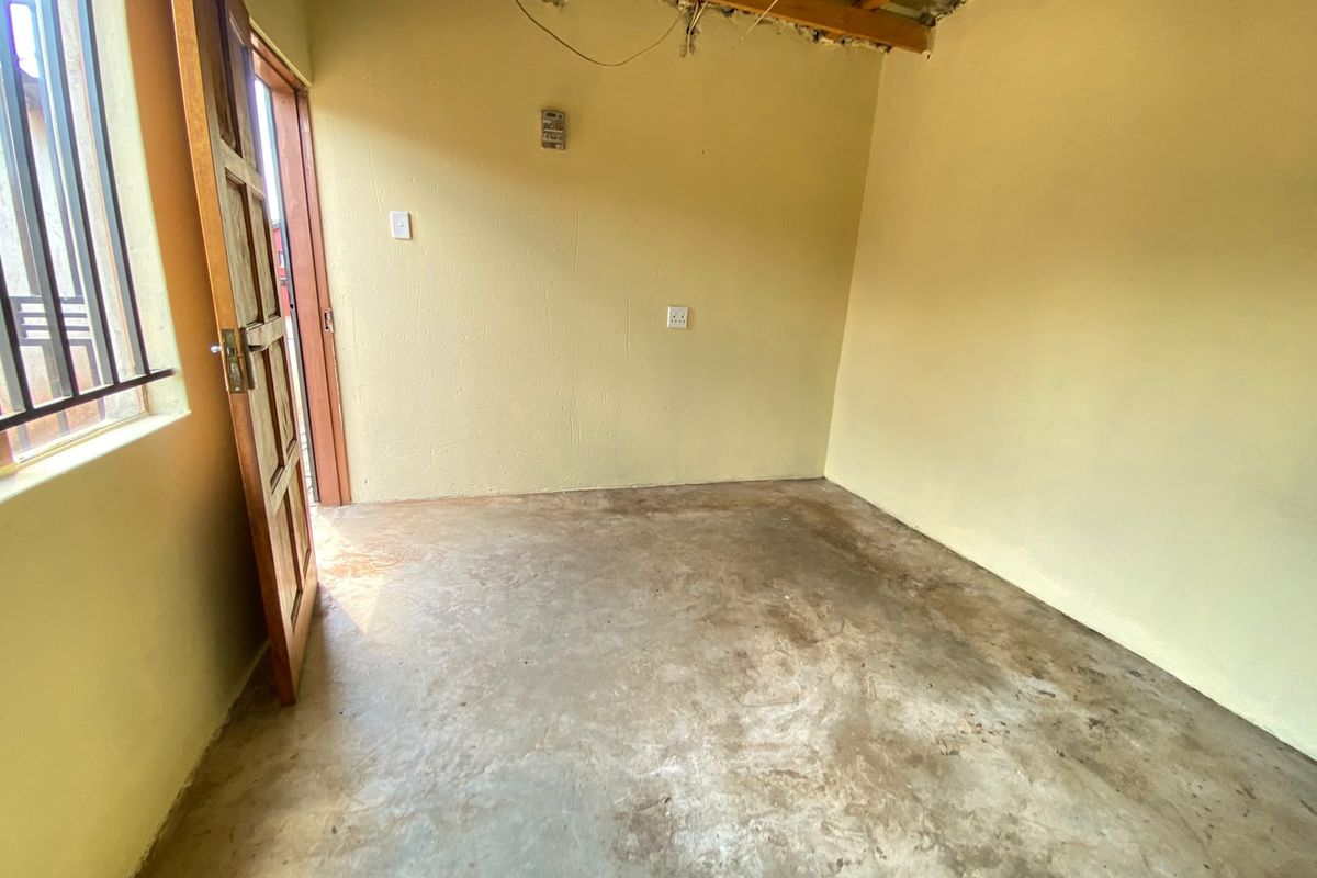 An unfinished bedroom space featuring exposed ceiling beams, concrete flooring, and a timber door, offering a blank canvas for renovation and interior finishing.