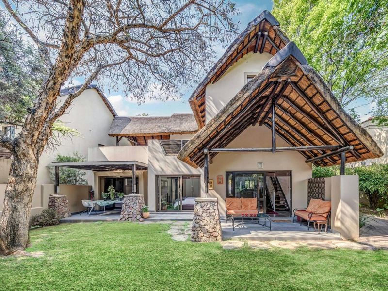 Rear view of a cluster home featuring a distinctive thatched roof, covered patio areas, stone-clad pillars, and a well-maintained private garden.