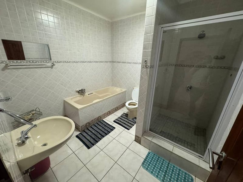 A functional bathroom featuring a built-in bathtub, separate shower enclosure, pedestal basin, and toilet with neutral ceramic wall and floor tiling.