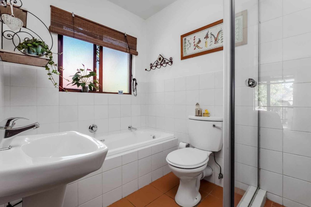 A functional bathroom featuring a pedestal sink, a built-in bathtub, a separate glass-enclosed shower, and white wall tiling.
