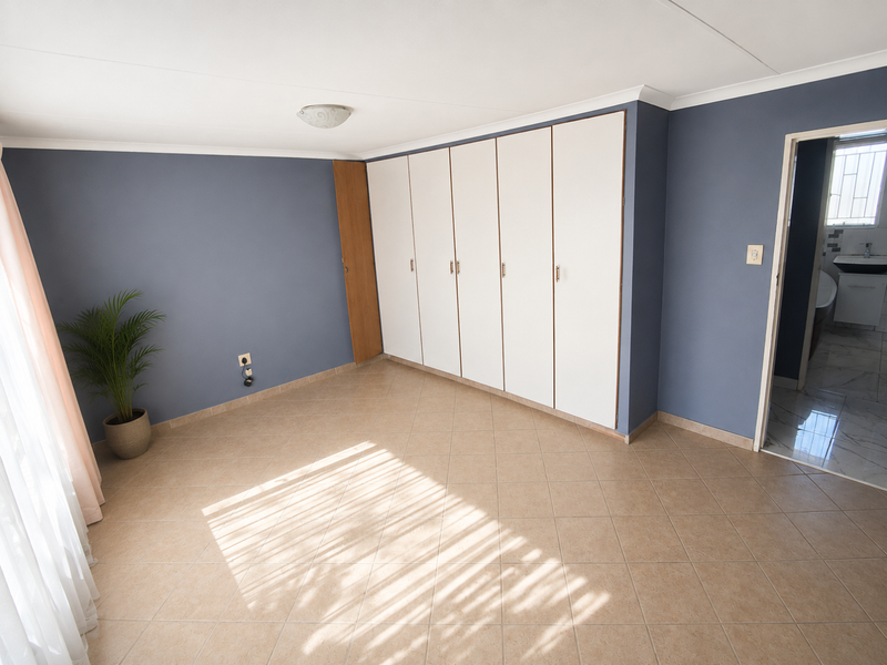 A spacious, empty bedroom featuring neutral tiled flooring, built-in cupboards, and direct access to an en-suite bathroom.