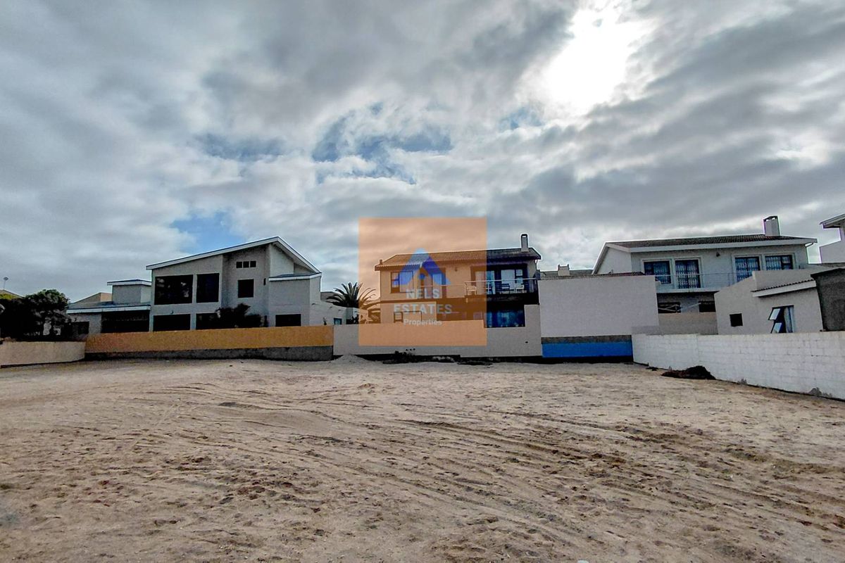 A vacant residential plot of land featuring sandy ground and surrounding boundary walls, situated in a developed neighborhood.