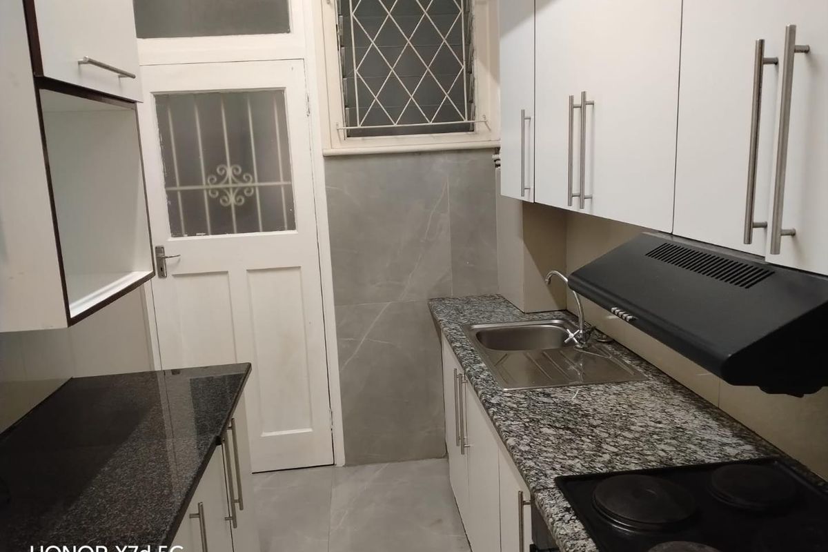 Compact kitchen featuring granite countertops, white cabinetry, built-in hob, extractor fan, and tiled finishes with a secure rear access door.