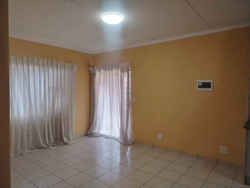 An empty living room featuring tiled flooring, neutral wall paint, and natural light through window and door curtains.