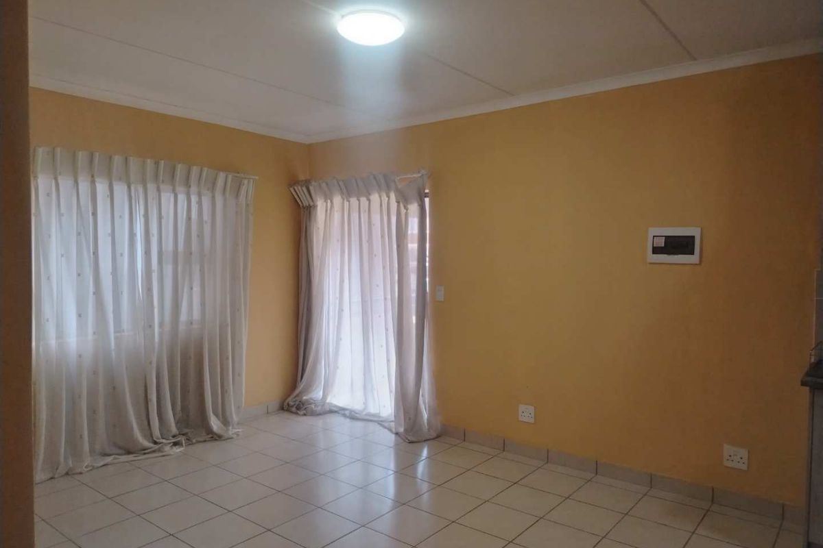 An empty living room featuring tiled flooring, neutral wall paint, and natural light through window and door curtains.