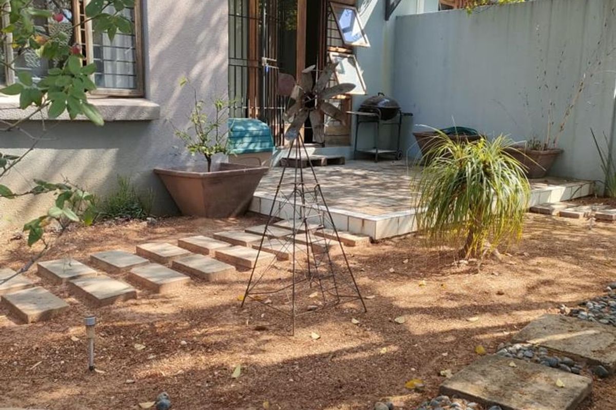 Rear exterior view of the apartment featuring a paved patio area, stepped stone pathway, and a metal balcony above.