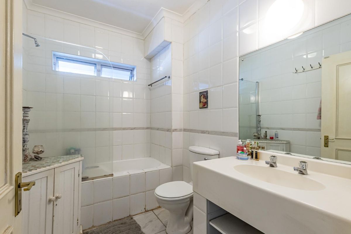 A functional bathroom featuring a built-in bathtub with shower, a vanity basin, and a toilet, finished with white wall tiles.