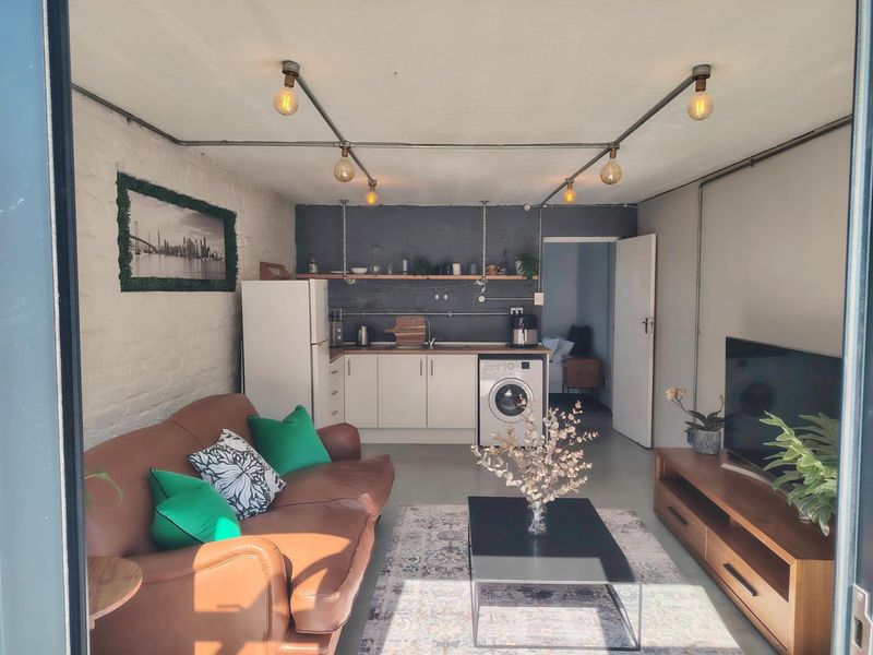 Open-plan living area featuring a compact kitchen with built-in cabinetry, exposed conduit lighting, and a modern industrial aesthetic with concrete flooring.
