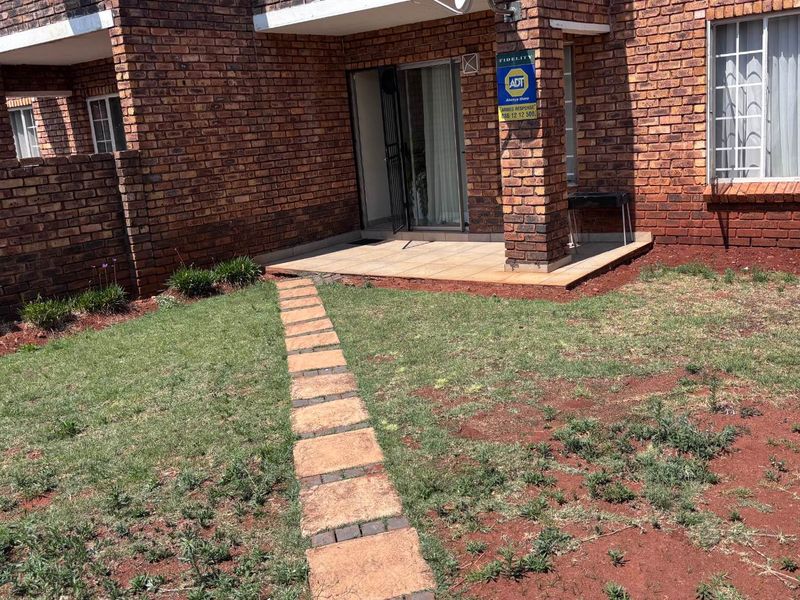Rear view of the apartment featuring a private garden with a stone pathway, a tiled patio area, and face-brick exterior walls.