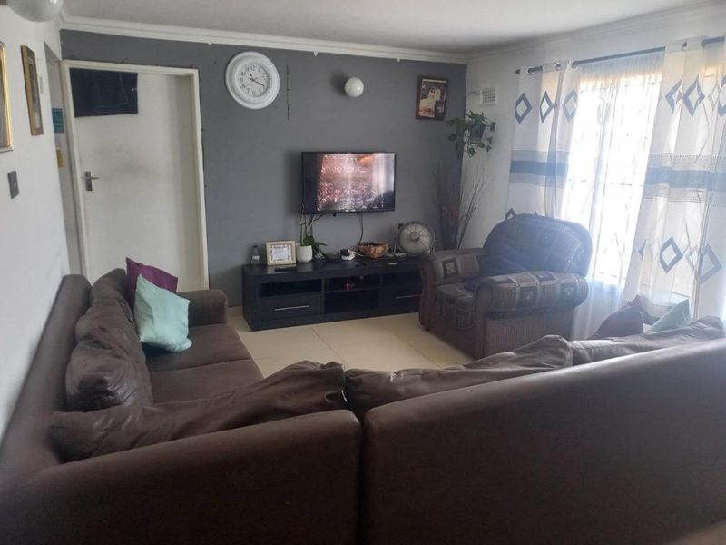 A functional living room featuring tiled flooring, coved ceiling details, and a neutral grey accent wall.