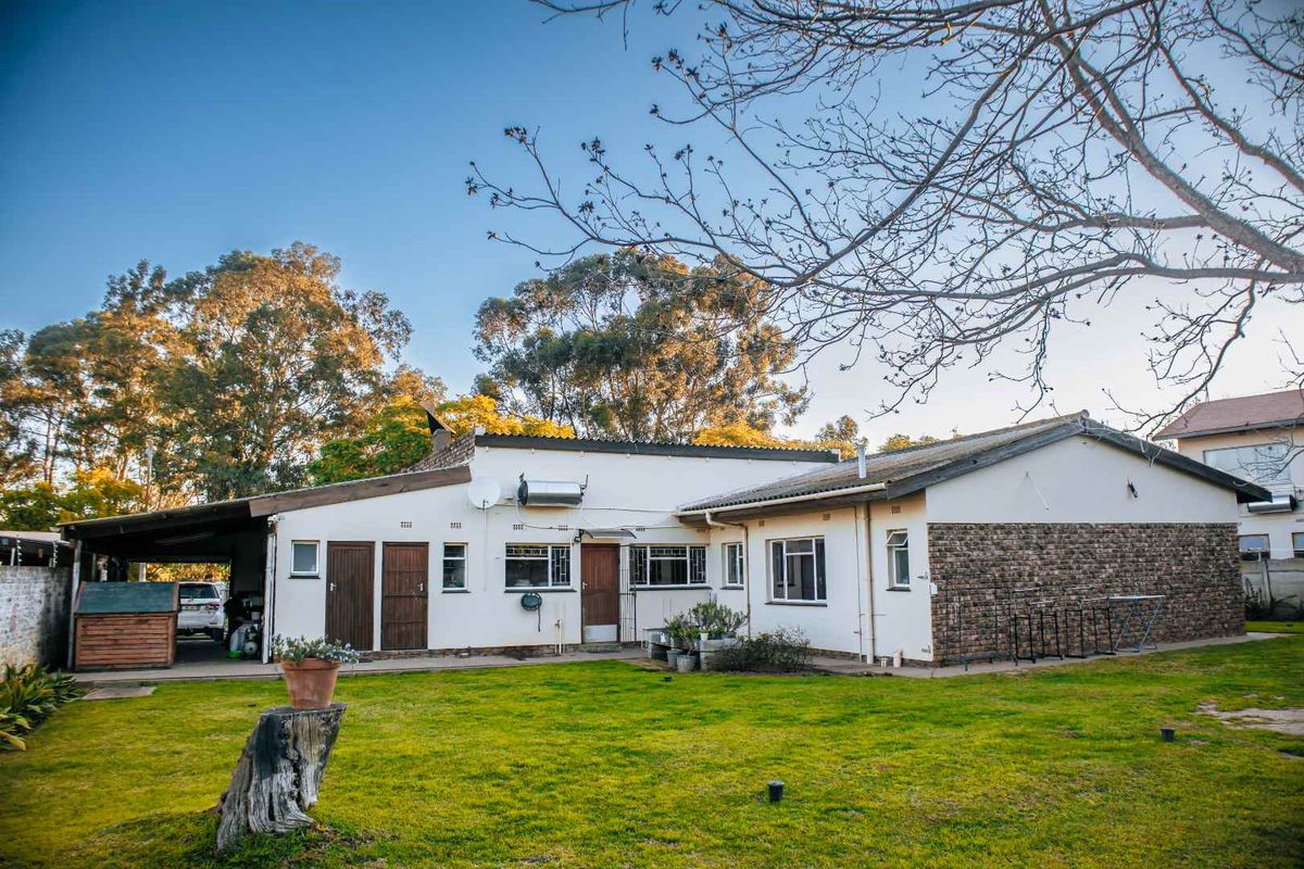 Rear view of the property featuring a lawn, stone-clad wall section, solar water heater, and an attached carport.
