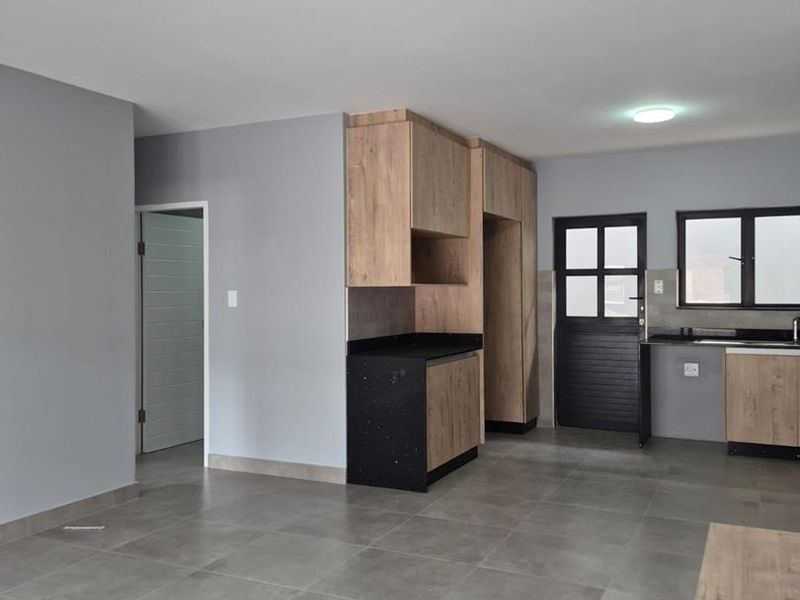 Modern open-plan kitchen featuring wood-finish cabinetry, dark stone countertops, and neutral grey floor tiles in a clean, vacant space.