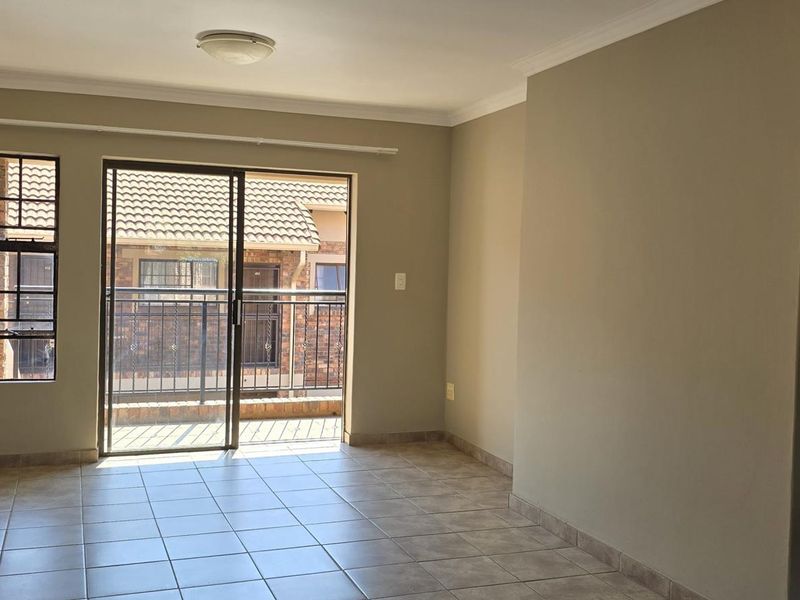An empty living room featuring neutral walls, tiled flooring, and a sliding glass door providing access to a balcony.