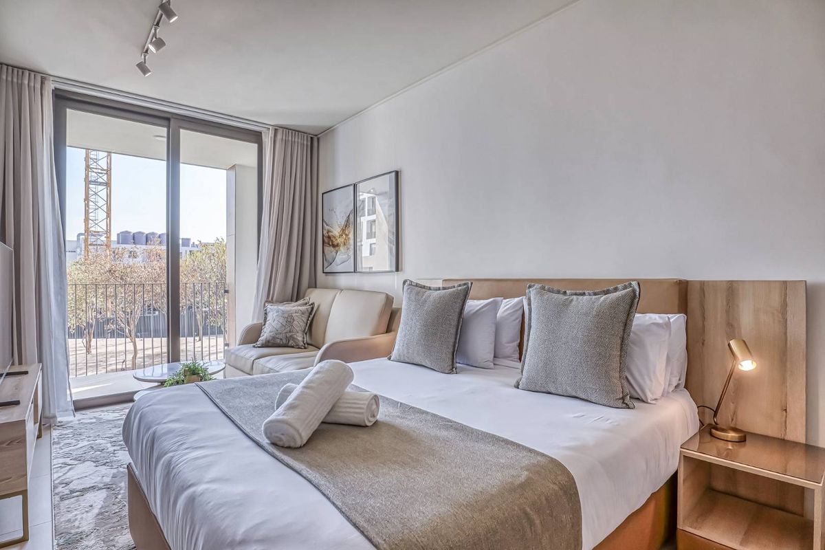 Modern bedroom featuring a built-in headboard, track lighting, and large sliding glass doors leading to a private balcony.