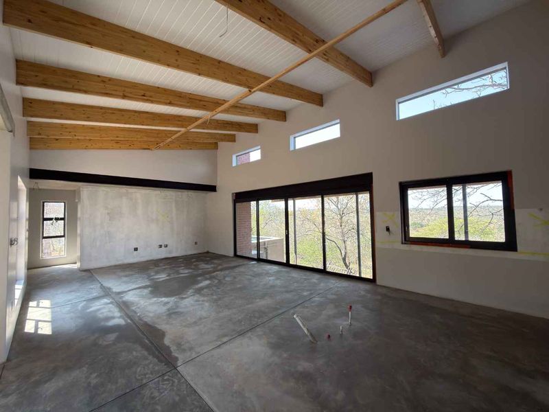 Spacious open-plan living area featuring exposed timber beams, concrete floors, and large sliding doors leading to an outdoor view.
