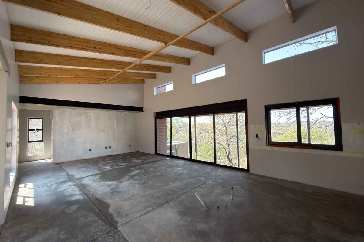Spacious open-plan living area featuring exposed timber beams, concrete floors, and large sliding doors leading to an outdoor view.