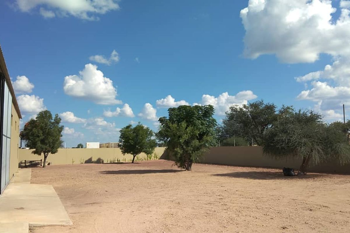 Spacious rear yard area featuring a corrugated metal industrial building, concrete apron, and secure perimeter wall with electric fencing.
