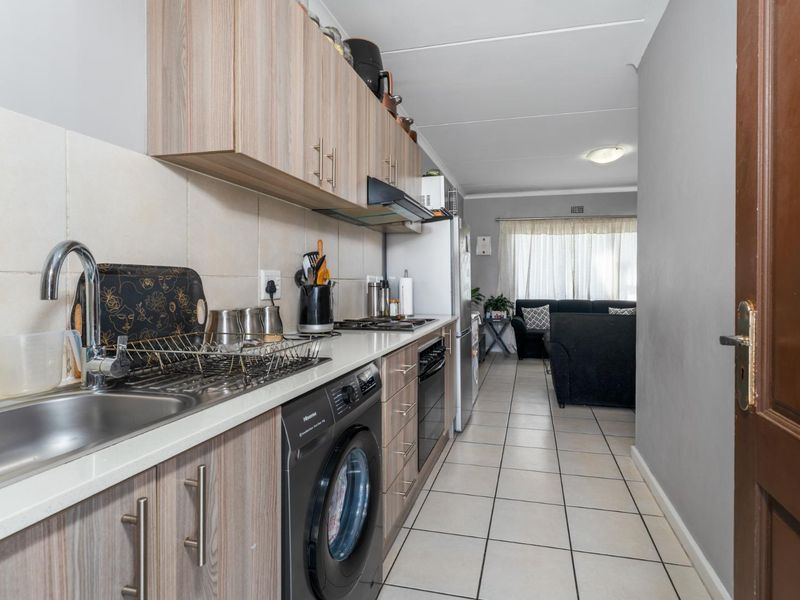 Open-plan kitchen featuring wood-look cabinetry, tiled flooring, and integrated appliances, flowing seamlessly into the adjacent living area.