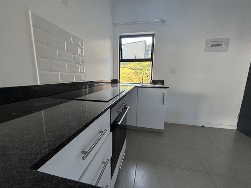 A modern, clean kitchen featuring granite countertops, subway tile backsplash, built-in oven and hob, and neutral tiled flooring.