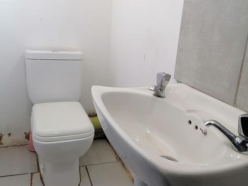 A compact bathroom featuring a white pedestal basin and toilet with tiled flooring and splashback, requiring minor maintenance and cosmetic updates.