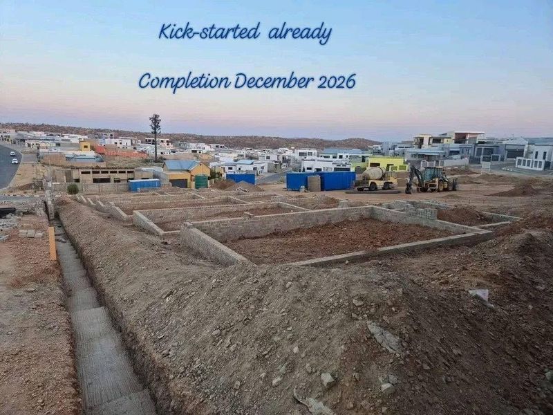 Construction site showing foundation work in progress for a new townhouse development, with completion scheduled for December 2026.