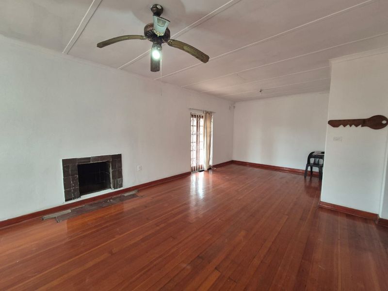 Spacious living room featuring polished hardwood flooring, a built-in fireplace, and a ceiling fan, offering a bright and open layout.