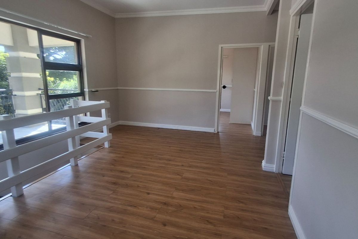An empty, well-maintained living area featuring laminate flooring, crown molding, and a sliding glass door leading to a balcony.