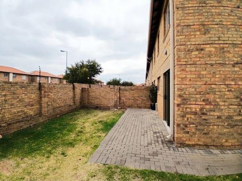 A private rear garden featuring a paved patio area, brick boundary walls with electric fencing, and direct access to the townhouse interior.