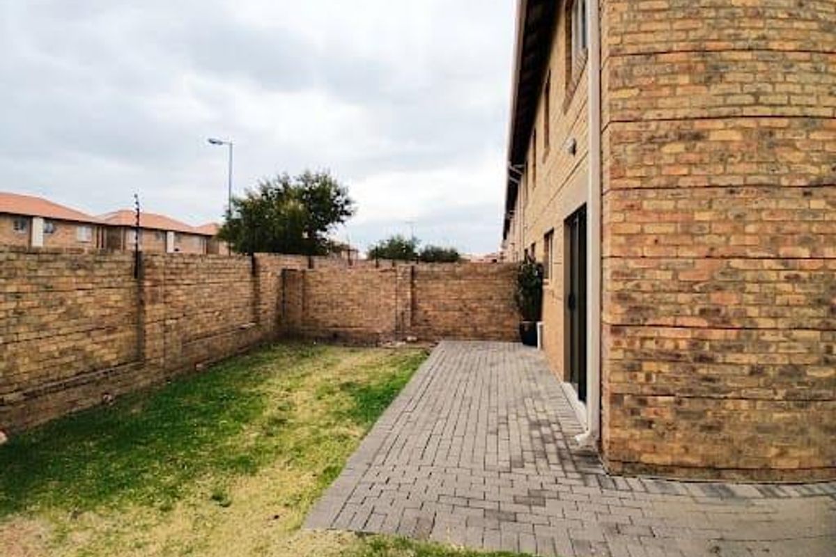 A private rear garden featuring a paved patio area, brick boundary walls with electric fencing, and direct access to the townhouse interior.