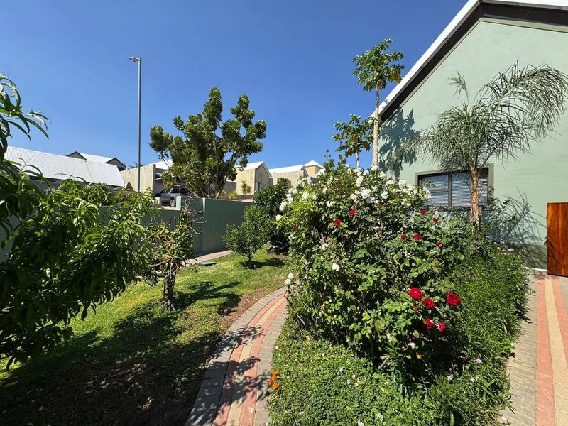 A well-maintained rear garden featuring a paved walkway, established shrubs, and a boundary wall alongside the house exterior.