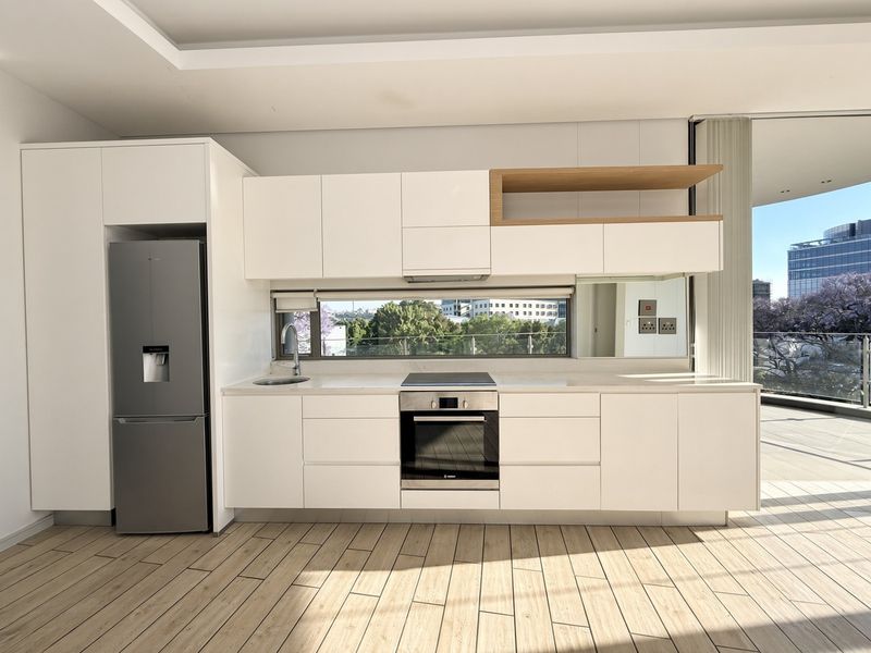 Modern, minimalist kitchen featuring sleek white cabinetry, stone countertops, integrated appliances, and wood-look tile flooring, with a large window offering natural light and views.