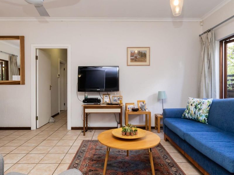 A comfortable living room featuring ceramic floor tiles, a ceiling fan, and natural light through a timber-framed window.