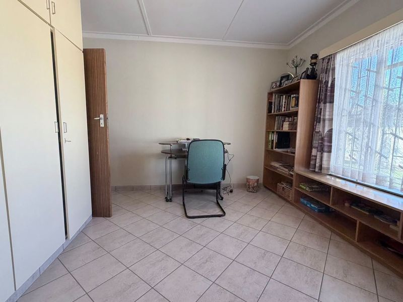 A functional bedroom featuring tiled flooring, built-in cupboards, and a window with security bars, offering a neutral space ready for personalization.