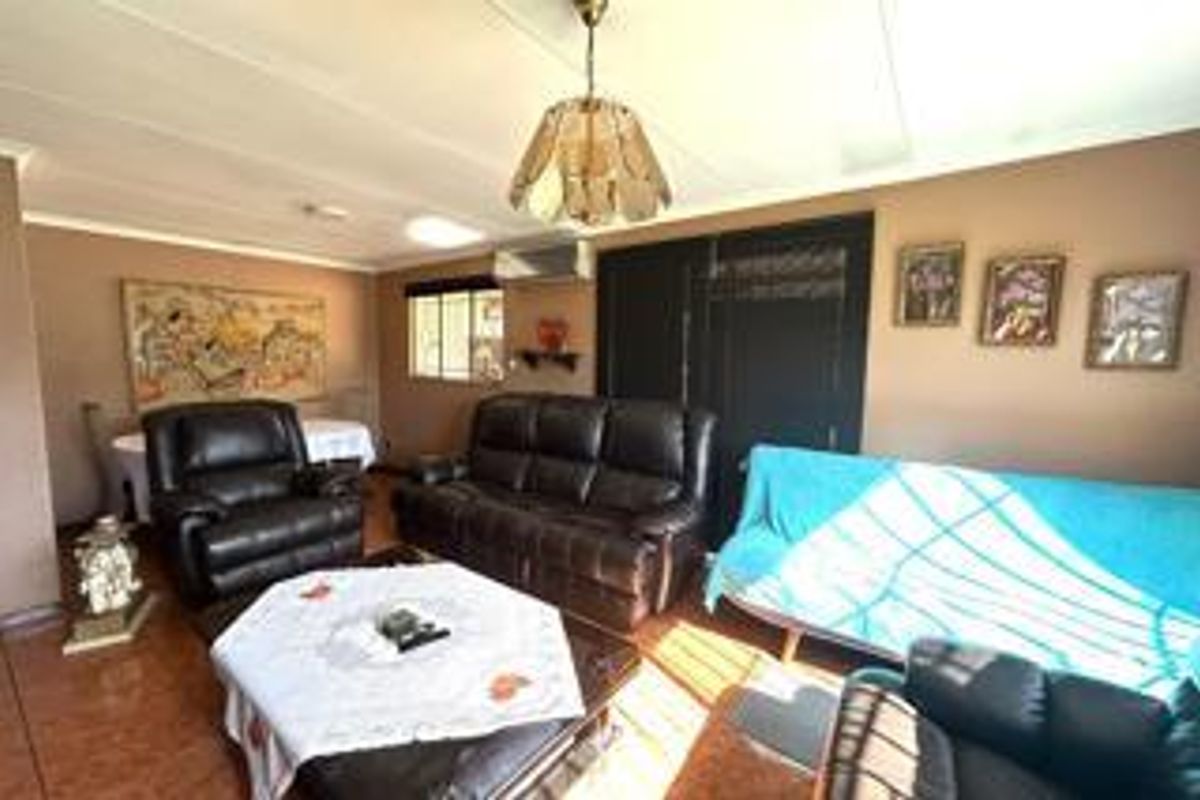A spacious living room featuring tiled flooring, a wall-mounted air conditioning unit, and a central pendant light fixture.