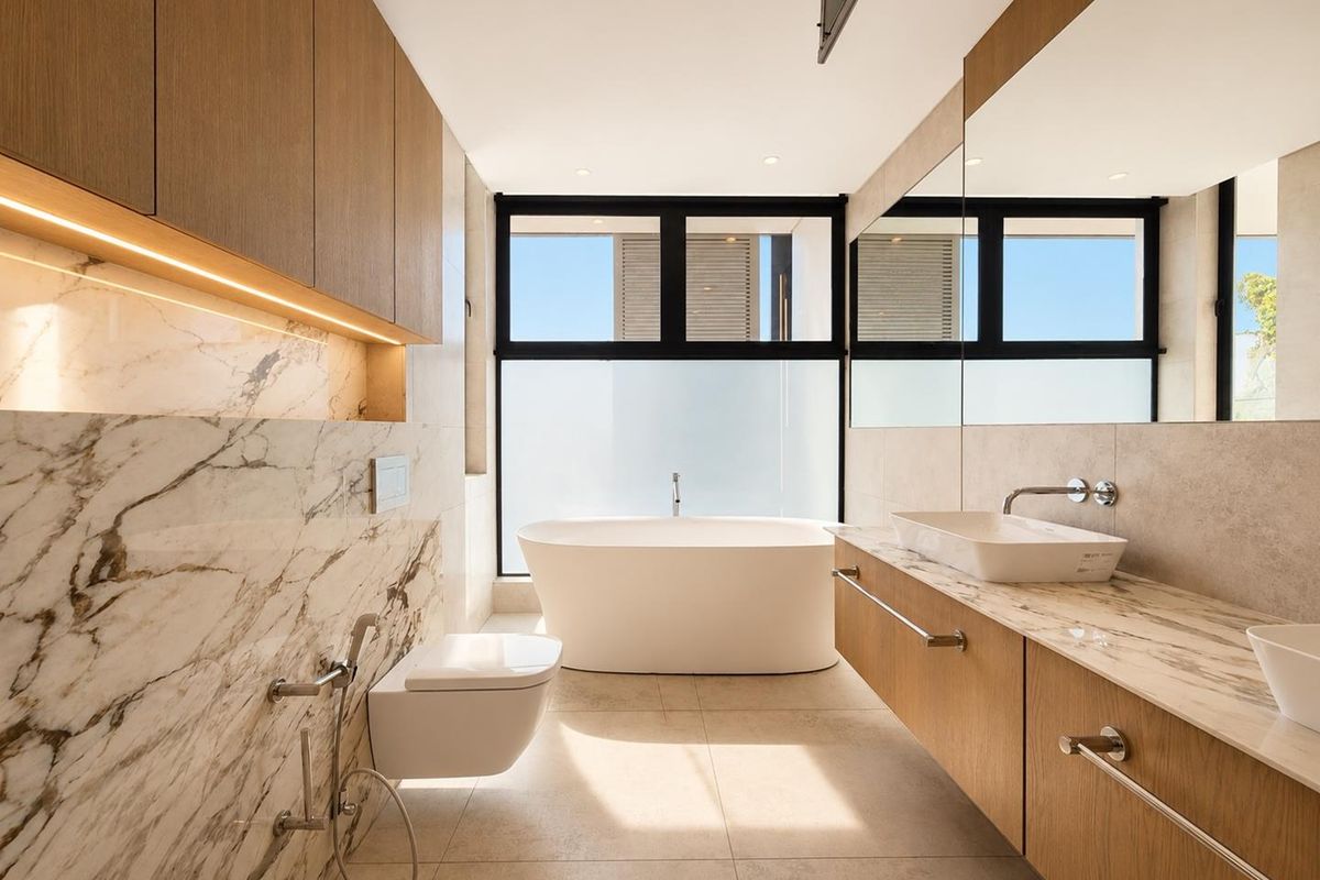 Modern luxury bathroom featuring a freestanding bathtub, wall-mounted toilet, double vanity with marble countertop, and elegant under-cabinet lighting.