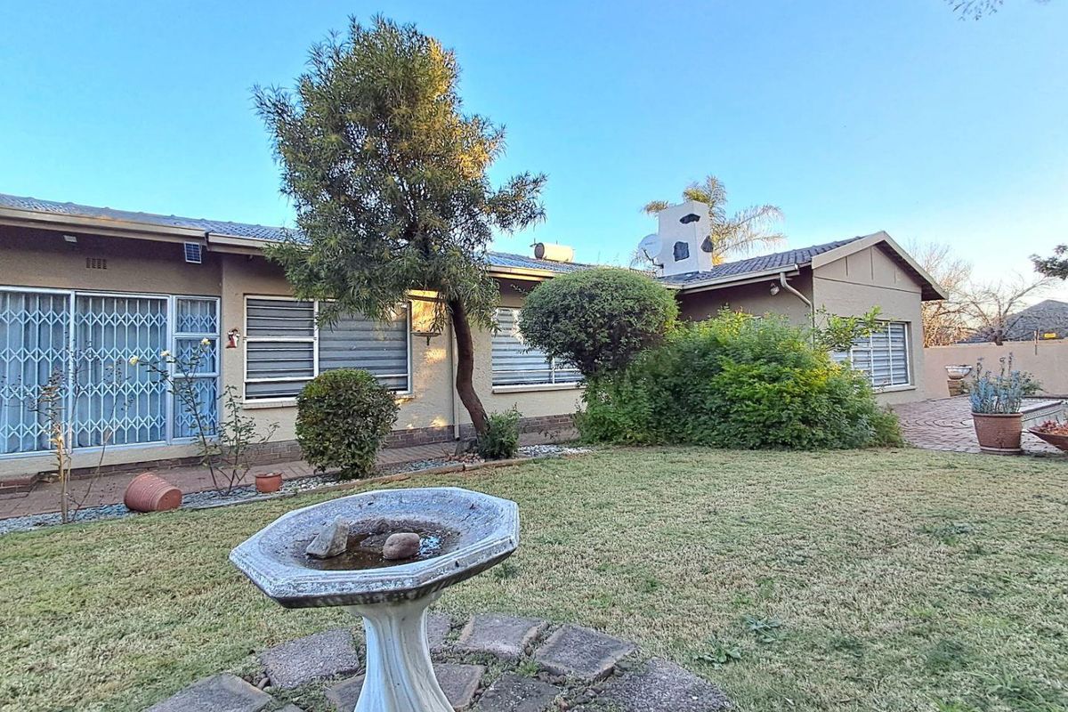 A view of the rear exterior of the house, featuring a landscaped garden, paved patio area, and established trees.