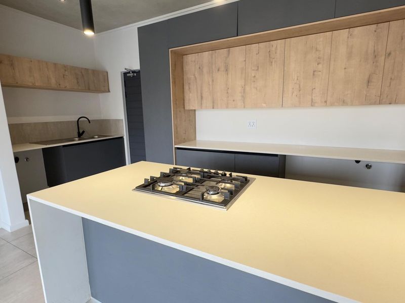 Modern kitchen featuring a central island with a gas hob, stone countertops, and contemporary two-tone cabinetry with integrated storage.