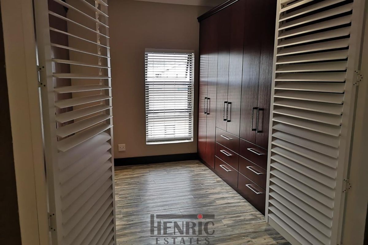 A clean, modern bedroom featuring extensive dark wood built-in cabinetry, wood-look laminate flooring, and white plantation-style shutters.