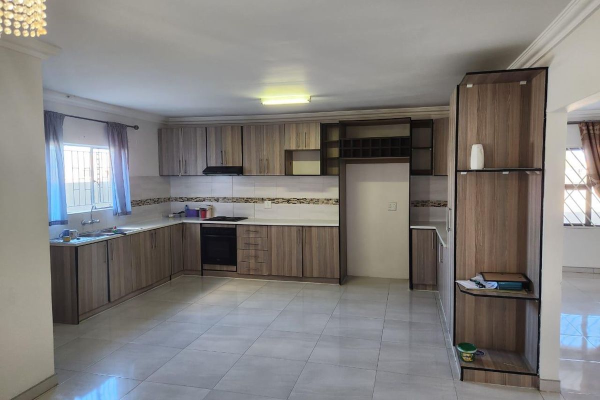 A spacious kitchen featuring modern wood-grain cabinetry, tiled flooring, a built-in oven, hob, and extractor fan with ample counter space.