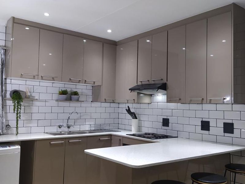Modern kitchen featuring high-gloss cabinetry, subway tile backsplash, stone countertops, and integrated appliances with a breakfast bar peninsula.