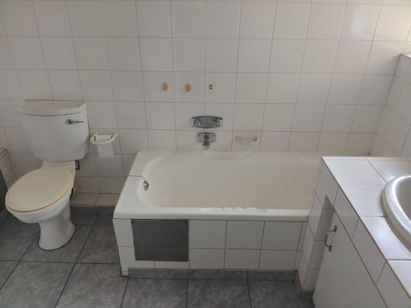 A dated bathroom featuring a built-in bathtub, toilet, and vanity basin with tiled walls and flooring, offering potential for modernization and renovation.