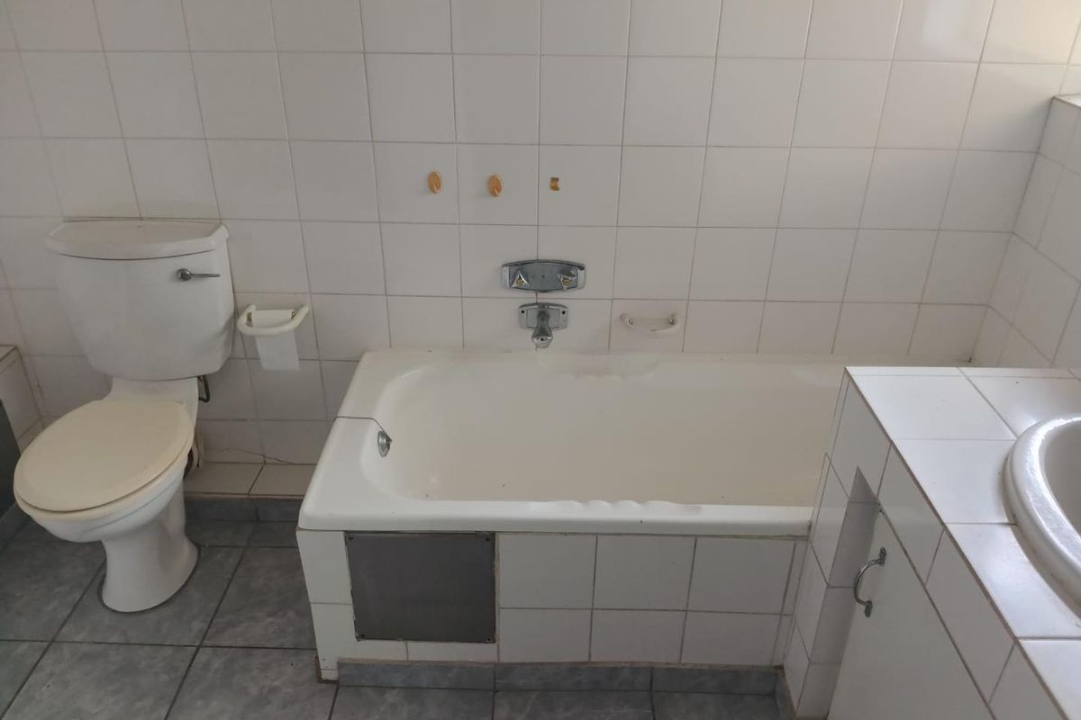 A dated bathroom featuring a built-in bathtub, toilet, and vanity basin with tiled walls and flooring, offering potential for modernization and renovation.