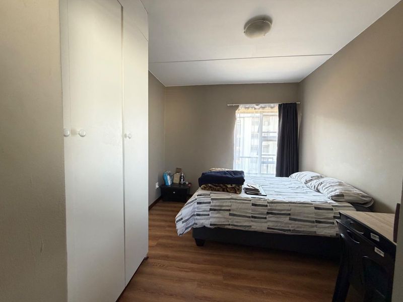 A functional bedroom featuring laminate flooring, a built-in wardrobe, and a window providing natural light.