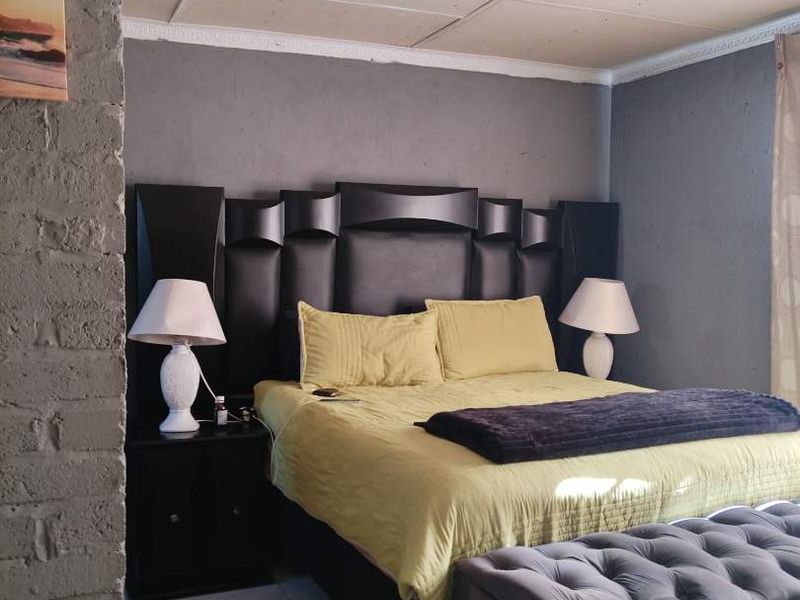 A bedroom featuring tiled flooring, an exposed brick accent wall, and a panelled ceiling.