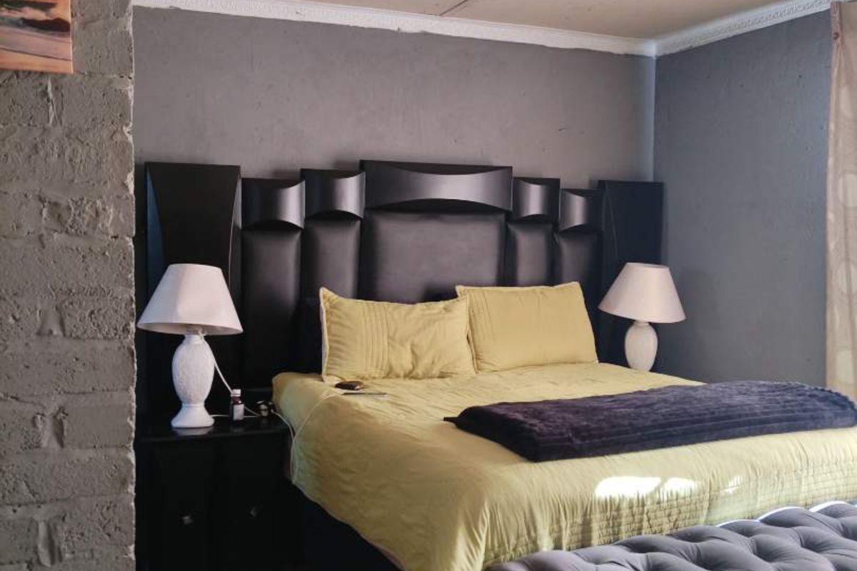 A bedroom featuring tiled flooring, an exposed brick accent wall, and a panelled ceiling.