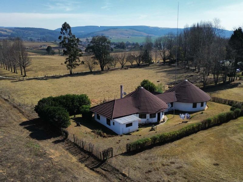 Aerial view of a farm property featuring a unique round-structure house with a tiled roof, set within expansive rural grounds and surrounding landscape.