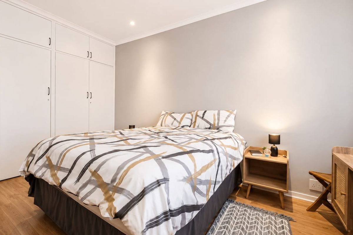 A well-maintained bedroom featuring laminate flooring, neutral walls, and ample built-in cupboard storage with recessed downlighting.