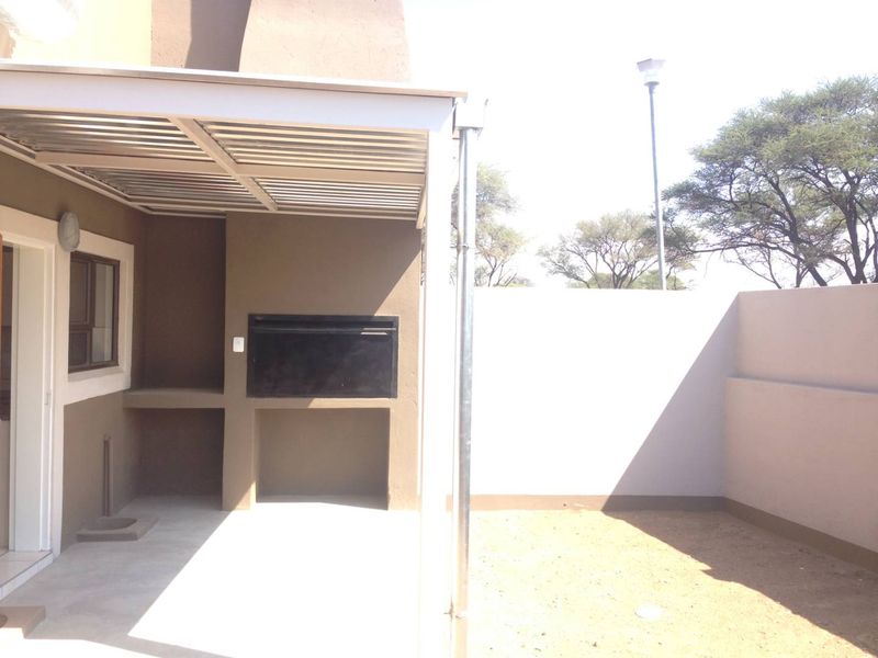 A covered patio area featuring a built-in braai, concrete flooring, and an adjacent private outdoor space with boundary walls.