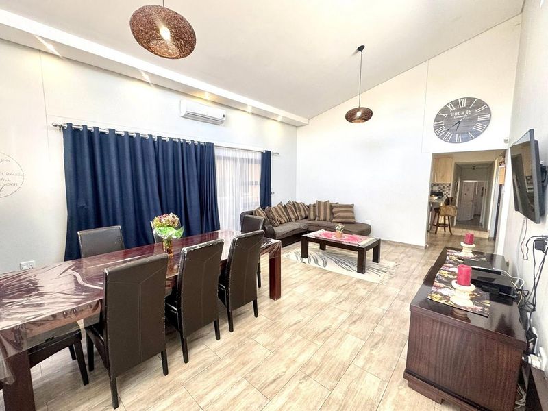 Spacious open-plan living and dining area featuring vaulted ceilings, tiled flooring, and a wall-mounted air conditioning unit.